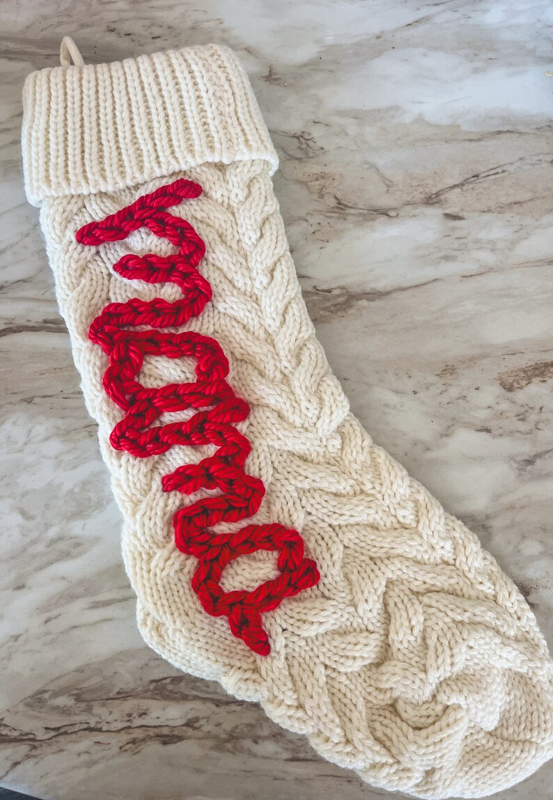 Peut inclure: Une chaussette de No&euml;l en tricot blanc avec un motif en tricot torsad&eacute; rouge qui &eacute;pelle "Santa".