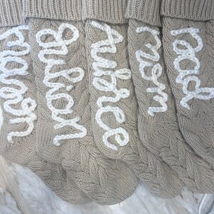 Peut inclure: Quatre chaussettes en tricot beige avec des noms brod&eacute;s en blanc : "Maman", "Papa", "Grand-m&egrave;re" et "Grand-p&egrave;re".