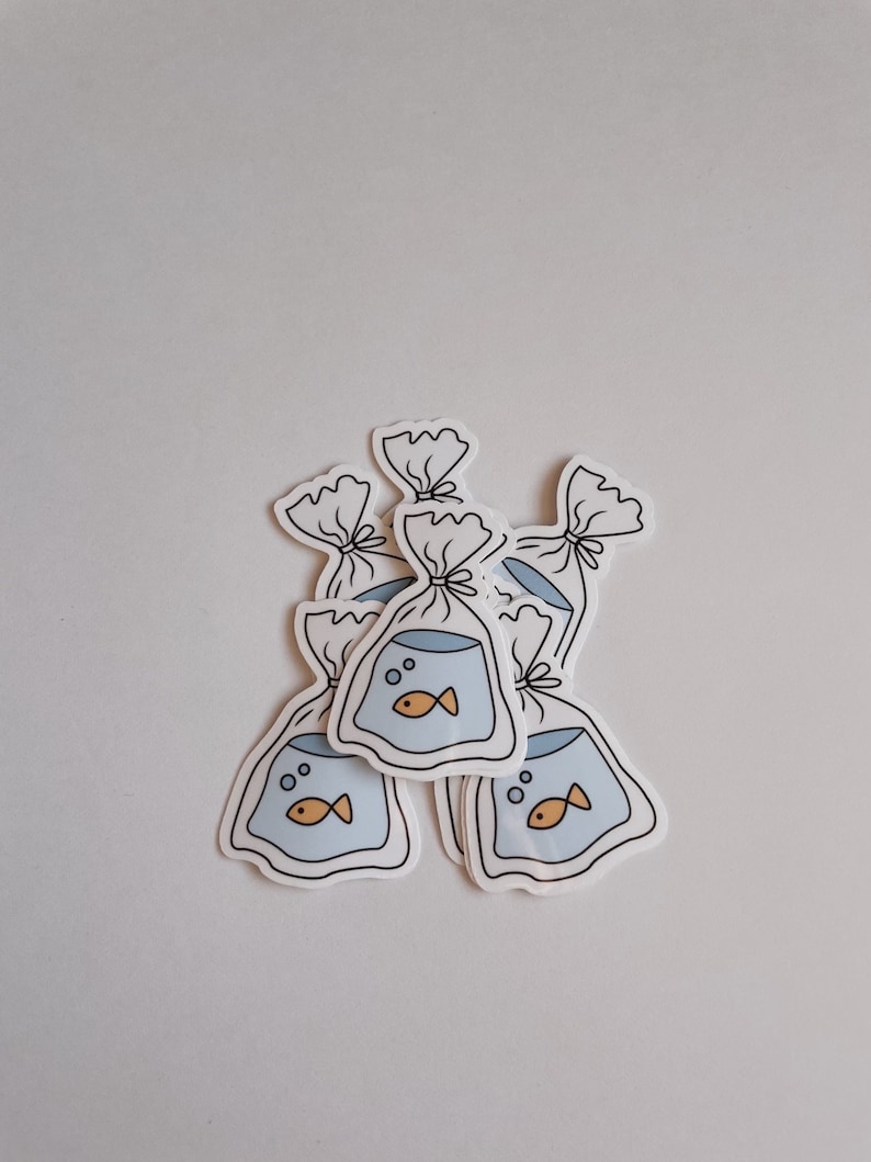 May include: Five white stickers with a cartoon drawing of a goldfish in a plastic bag. The goldfish is orange and has a black outline. The plastic bag is blue and has a white outline. The stickers are arranged in a pile.