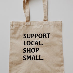 May include: A beige canvas tote bag with black text that reads "SUPPORT LOCAL. SHOP SMALL."