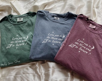 May include: Three t-shirts with a space-themed graphic and the text "Love you to the Moon and to Saturn." The shirts are in green, blue, and burgundy.