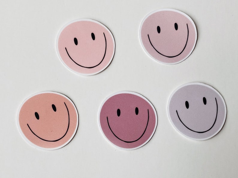 May include: Five round stickers with smiley faces in various shades of pink, purple, and peach.