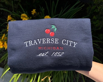 May include: Navy blue sweatshirt with a red embroidered cherry design and the text "Traverse City, Michigan est. 1852".