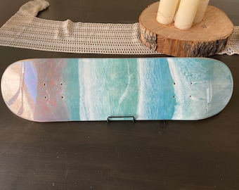 May include: A white skateboard deck with a blue and green ocean wave design. The deck is painted with a light blue, turquoise, and white color scheme, creating a realistic ocean wave effect.