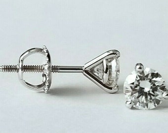 May include: A pair of diamond stud earrings. The earrings have round-cut diamonds set in a prong setting. The earring posts and backs are made of silver-coloured metal. The earrings are displayed on a white background. The diamonds sparkle.