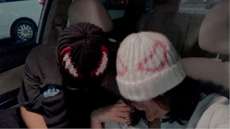 Puede incluir: Dos gorros de punto hechos a mano. Uno es negro con un dise&ntilde;o rojo y blanco, el otro es blanco con un dise&ntilde;o rosa. Los gorros son probablemente para el invierno y est&aacute;n en un coche.