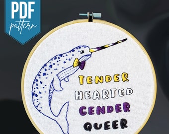 May include: Embroidered hoop art featuring a narwhal with a purple and yellow bow tie. The narwhal is surrounded by the text "Tender Hearted Gender Queer" in a variety of colours.