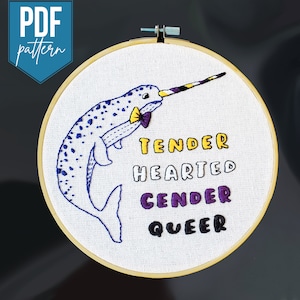 May include: Embroidered hoop art featuring a narwhal with a purple and yellow bow tie. The narwhal is surrounded by the text "Tender Hearted Gender Queer" in a variety of colours.