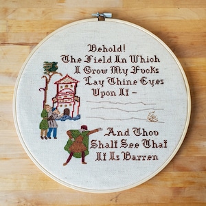 An embroidery hoop with a cross stitched design of 3 people looking at a field with a house and bird in the background. Text reads: Behold! The Field In Which I Grow My Fvcks. Lay Thine Eyes Upon It - And Thou Shalt See That It Is Barren.