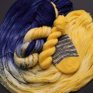 May include: A collection of yarn in shades of yellow and blue. The yarn is arranged in a circular pattern, with the yellow yarn in the centre and the blue yarn around the edges. There is also a small knitted sock in the centre of the yarn.