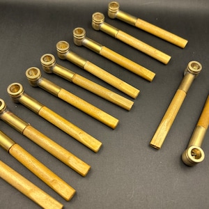 May include: A set of ten brass smoking pipes with wooden stems. The pipes are arranged in a fan shape on a black surface.