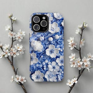 Può includere: Una custodia per telefono blu e bianca con fiori e un ritaglio per la fotocamera. La custodia presenta un design dettagliato di fiori bianchi su uno sfondo blu.