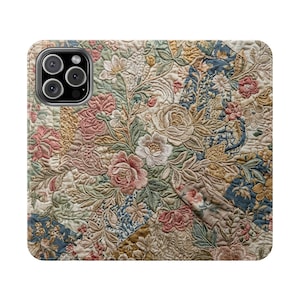 May include: A phone case featuring a detailed floral pattern reminiscent of a vintage quilt. The design incorporates various colors, including pink, cream, green, and blue, with a textured, embroidered appearance. The case has a camera module.