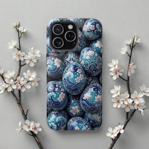 May include: A phone case with a repeating pattern of blue and teal decorative eggs with floral and wave designs. The case has a glossy finish and a camera cutout. White flowers and branches are in the background.