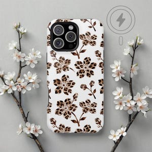 May include: White phone case with a brown floral leopard print design. The case has a camera cutout and a wireless charging symbol. The background features white flowers and branches.