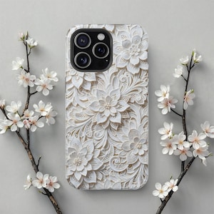 May include: A white floral-patterned phone case with a raised, textured design. The case features a detailed, three-dimensional floral pattern with multiple flower shapes and intricate details. The case is surrounded by white flowers on branches.