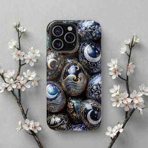 May include: A phone case with a repeating pattern of decorated eggs in blue, gold, and black. The eggs feature celestial and floral designs, including moons, stars, and flowers. The case has a glossy finish and a camera cutout.