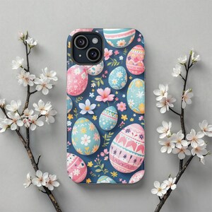 Puede incluir: Una funda para smartphone con fondo azul oscuro decorada con un patrón repetitivo de huevos de Pascua coloridos en tonos rosa, azul claro y amarillo, intercalados con pequeñas flores blancas y rosas y hojas verdes.