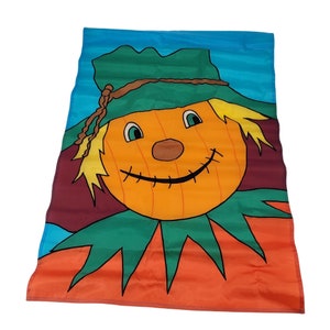 May include: A garden flag with a smiling scarecrow design. The scarecrow has an orange face, green hat and collar, and a stitched mouth. The background features blue, burgundy, and orange sections. The flag is made of a smooth, shiny material.