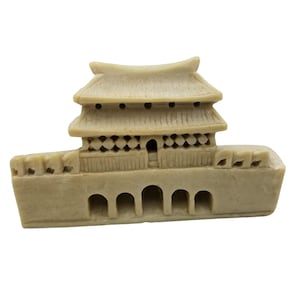 May include: A small, beige, ceramic figurine of a traditional Asian temple with a curved roof and intricate details. The temple has a series of arches at the base.