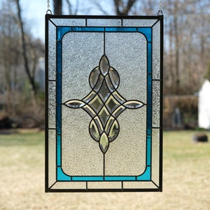May include: A stained glass window with a geometric design in shades of blue and clear glass. The window is framed in black metal and has a textured glass surface.