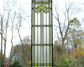 May include: A stained glass window panel with a geometric design featuring green and white glass. The panel is hanging from a chain and is framed in black.