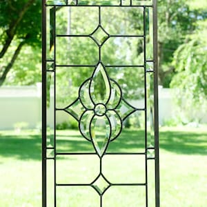May include: A stained glass window panel with a geometric design featuring a diamond shape with a floral pattern in the center. The glass is clear and the lead cames are black.