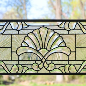 May include: A stained glass window panel with a geometric design featuring a fan-shaped pattern in the center. The panel is made of clear glass with black lead cames.