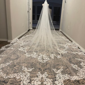 May include: A long white bridal veil with delicate lace trim. The veil is made of soft tulle and features a scalloped edge.