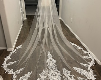 Puede incluir: Un velo de novia largo y blanco con un delicado borde de encaje floral. El velo está hecho de tul suave y tiene una longitud de catedral.