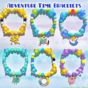 Könnte beinhalten: Sechs farbenfrohe Armbänder mit Adventure Time-Charmanhängern. Die Armbänder haben gelbe, blaue, grüne und lila Perlen mit sternförmigen und runden Perlen. Jedes Armband hat einen anderen Adventure Time-Charmanhänger.