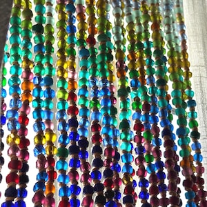 May include: A hanging curtain composed of multiple vertical strands of multicolored glass beads. The beads feature a variety of translucent and opaque hues, including blue, green, yellow, red, and pink, all strung together on thin, light-colored cord.