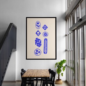 Puede incluir: Una impresi&oacute;n de arte mural rectangular en un marco negro con un fondo beige y una disposici&oacute;n vertical de iconos gr&aacute;ficos azules que incluyen flores, hojas y formas geom&eacute;tricas. El dise&ntilde;o consta de ocho formas azules distintas.