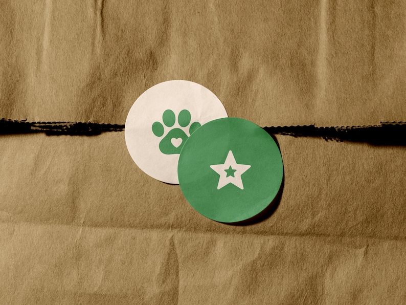 May include: Two circular stickers are layered on top of each other. The bottom sticker is white with a green paw print icon featuring a small heart in the center. The top sticker is green with a white five-pointed star icon in the center.