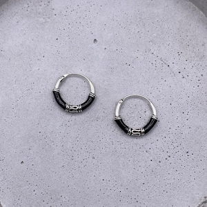 May include: Two silver hoop earrings with black accents on a grey concrete surface.