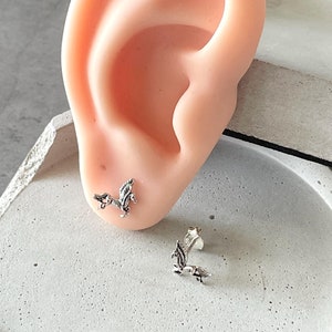Puede incluir: Un par de pendientes de plata con un delicado diseño de hojas. Los pendientes se muestran en la oreja de un maniquí.