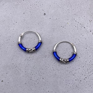 May include: A pair of silver hoop earrings with a blue enamel band. The earrings are small and delicate.