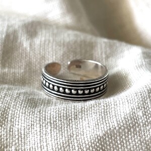 May include: A silver adjustable ring with a beaded design. The ring has three rows of beads, with the middle row being larger than the top and bottom rows.