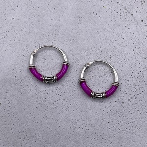 May include: A pair of silver hoop earrings with a purple enamel band around the hoop.