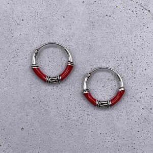Może przedstawiać: Para srebrnych kolczyków koła z czerwonymi akcentami emaliowanymi. Kolczyki są proste i eleganckie.