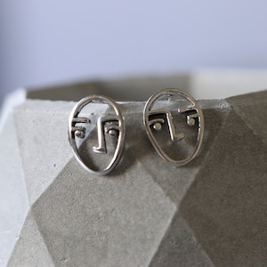 May include: A pair of silver earrings with a face design. The earrings are small and delicate, and they would make a great gift for someone who loves minimalist jewelry.