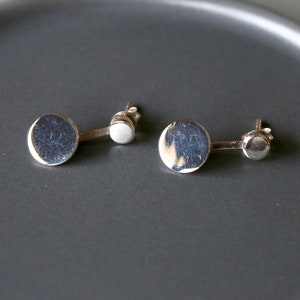 May include: A pair of silver earrings with a round disc shape. Each earring has a smaller round disc attached to the back.