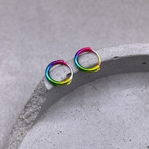 Puede incluir: Un par de pendientes de aro arcoíris. Los pendientes son de metal y tienen un acabado brillante.