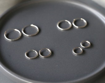Puede incluir: Un conjunto de seis pendientes de aro plateados de diferentes tamaños, expuestos sobre una superficie gris.