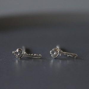 Könnte beinhalten: Ein Paar silberne Schlüssel-Ohrstecker. Die Ohrringe sind klein und zart und wären ein tolles Geschenk für einen Freund oder eine geliebte Person.