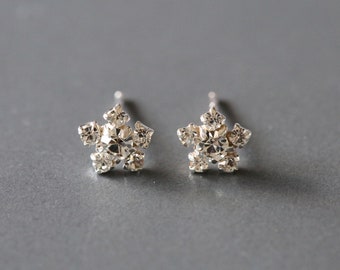 Puede incluir: Un par de pendientes de botón de copo de nieve plateados con diamantes de imitación transparentes.