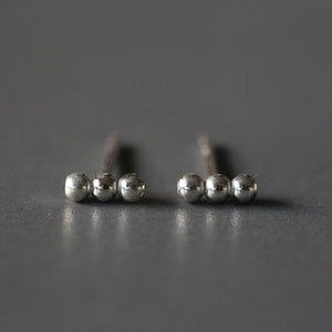 May include: A pair of silver stud earrings with three small round beads.