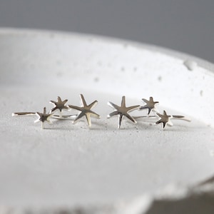 Puede incluir: Pendientes de plata con forma de estrella con tres estrellas en cada pendiente. Las estrellas están dispuestas en forma escalonada.