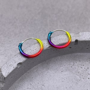 Könnte beinhalten: Ein Paar Regenbogen-Hoop-Ohrringe. Die Ringe sind silberfarben und haben einen Farbverlauf von Blau bis Rot.