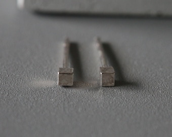 May include: A pair of silver earrings with small square-shaped charms.